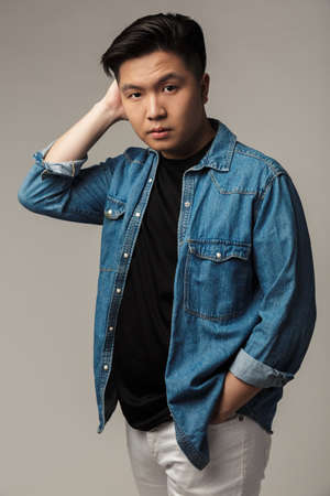 Image of confident handsome asian man posing and looking at camera isolated over gray background