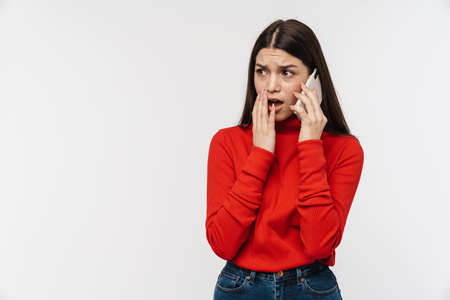 Photo of scared caucasian woman expressing shock while talking on mobile phone isolated over white...