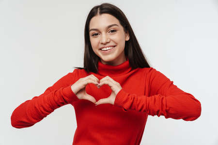 Photo of happy young woman smiling and showing heart with fingers isolated over white wallの写真素材