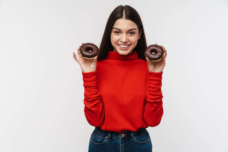 Photo of cheerful brunette woman smiling and holding chocolate donuts isolated over white backgroundの写真素材