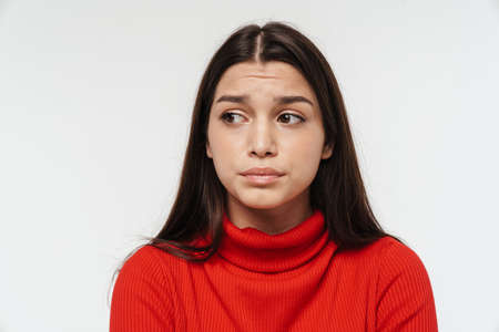 Portrait of a pretty upset young brunette woman wearing casual clothing isolated over white background, looking awayの写真素材