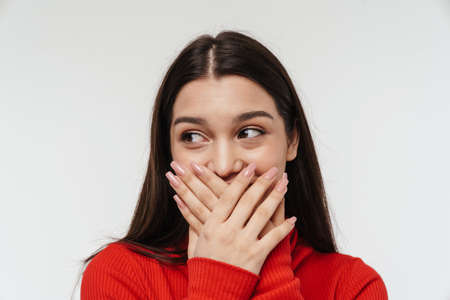 Portrait of a pretty cheerful young brunette woman wearing casual clothing isolated over white background, covers mouthの写真素材