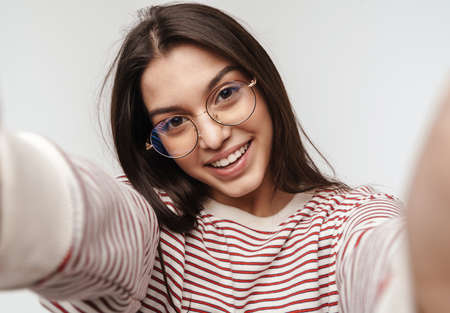 Photo of happy brunette young woman wearing eyeglasses smiling at camera isolated over white backgroundの写真素材
