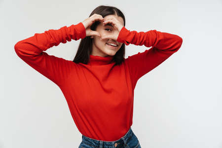 Photo of happy young woman smiling and showing heart with fingers isolated over white wallの写真素材