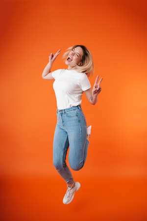 Image of joyful attractive woman showing peace sign while jumping isolated over orange background