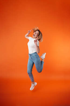 Image of joyful attractive woman showing peace sign while jumping isolated over orange background