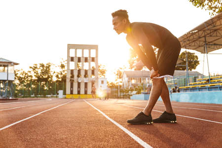 Image of muscular african american man running on sports stadium outdoors