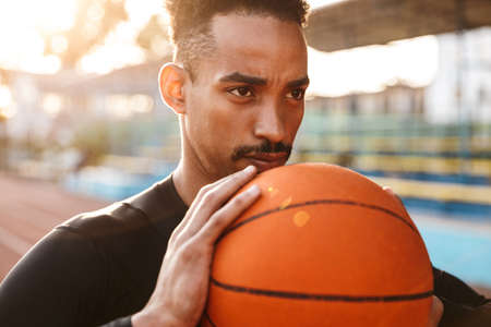 Image of a strong concentrated african handsome young sports man at stadium outdoors holding...