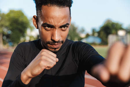 Image of focused african american man clenching fists and boxing on sports ground outdoorsの写真素材