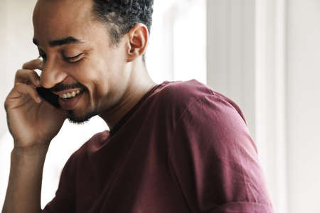 Photo closeup of joyful african american man smiling and talking on cellphone at home