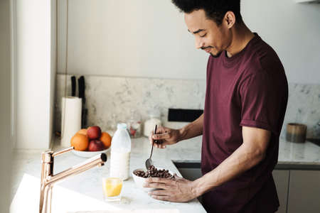 Photo of smiling african american man with beard preparing breakfast in kitchen at home
