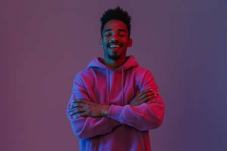 Portrait of smiling african american man in colorful hoodie poising on camera with his arms crossed...