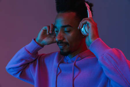 Portrait of calming african american man in colorful hoodie listening to music with headphones...