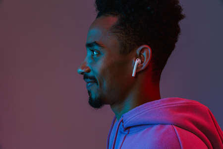 Portrait in profile of positive african american man in colorful hoodie listening to music with...