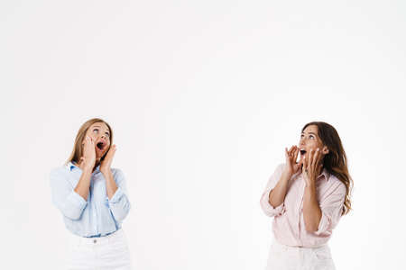Image of excited caucasian two women screaming and looking upward isolated over white backgroundの写真素材