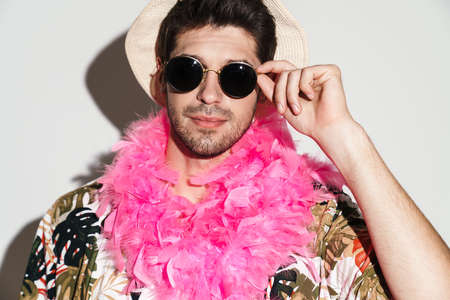 Portrait of handsome pleased man wearing sunglasses posing and looking at camera isolated over white...