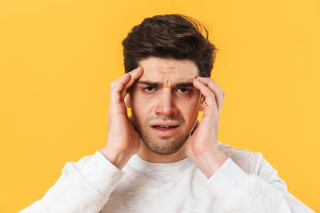 Photo of sick unhappy man having headache and touching his temples isolated over yellow background