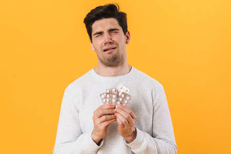 Photo of bristle unhappy man with allergy posing with medicine and crying isolated over yellow...