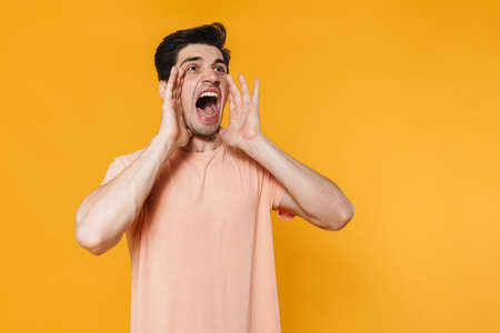 Photo of furious handsome man screaming with throwing up hands isolated over yellow background