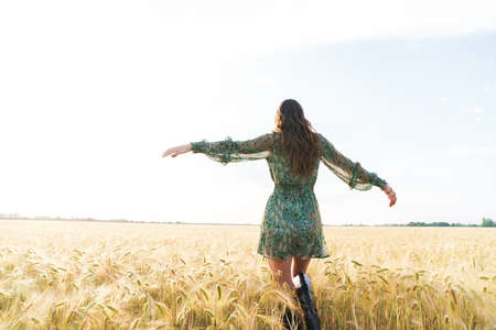 Photo from back of cute brunette woman in stylish dress dancing on wheat field at summer dayの写真素材
