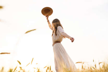 Photo of beautiful happy woman with straw hat dancing on wheat field at summer dayの写真素材