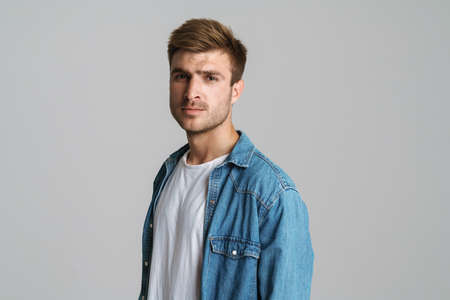 Portrait of brutal unshaven man posing and looking at camera isolated over grey background