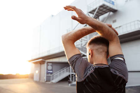 Image of athletic caucasian sportsman in earphones doing exercise while working out at urban area...