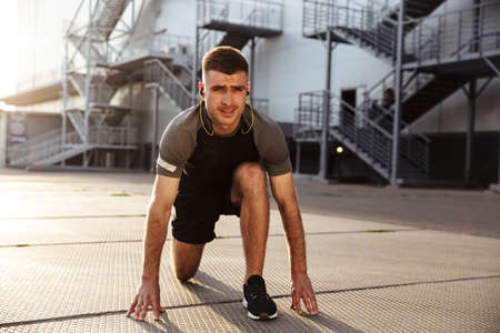 Image of unshaven caucasian sportsman in earphones doing exercise while working out at urban area...