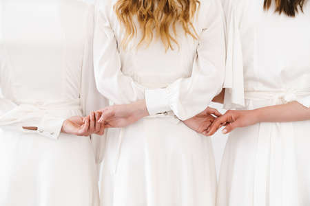 Cropped photo from back of three women in dresses holding hands together isolated over white wallの写真素材
