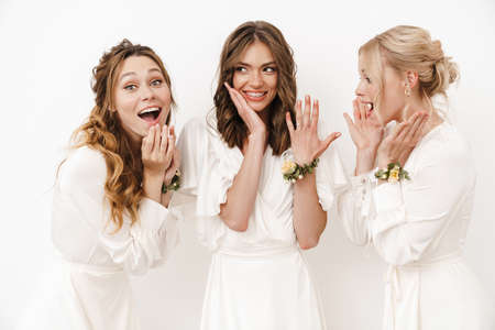 Photo of attractive happy bride showing her wedding ring at excited bridesmaids isolated over white wallの写真素材