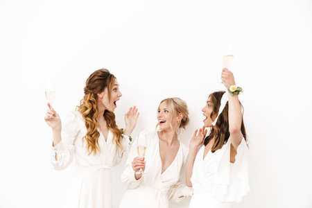 Photo of delighted young bridesmaids dancing and drinking champagne isolated over white wallの写真素材