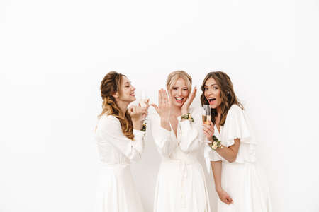 Photo of attractive happy bride showing her wedding ring at excited bridesmaids isolated over white wallの写真素材