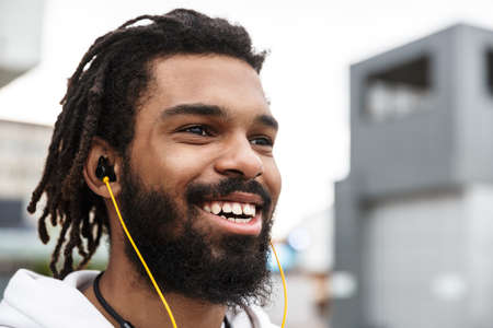 Picture of a cheery positive young man walking outdoors while listening music with earphonesの写真素材