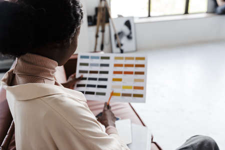 Back view photo of young african woman interior designer sitting on sofa indoors at home while...