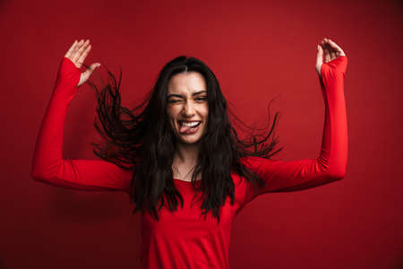Photo of brunette funny woman grimacing with throwing up hands isolated over red backgroundの写真素材