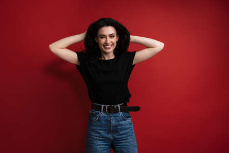 Photo of young cheerful woman in casual t-shirt laughing and grabbing her head isolated over red backgroundの写真素材