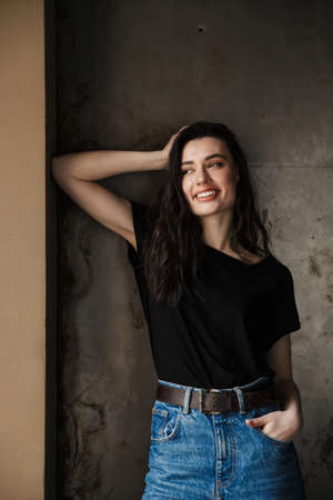 Photo of beautiful young brunette woman smiling and looking aside isolated over dark background