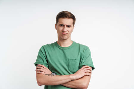 Image of disappointed caucasian man in basic t-shirt frowning and standing with arms crossed...