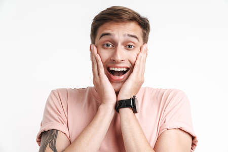 Image of excited caucasian man in basic t-shirt smiling and grabbing his face isolated over white...