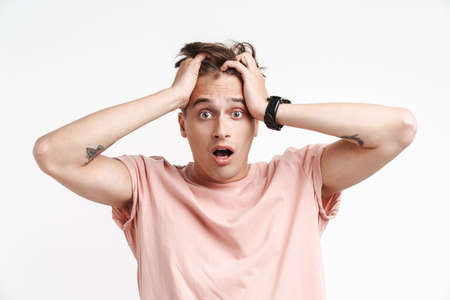 Image of scared caucasian man in basic t-shirt being stressed and grabbing his head isolated over...