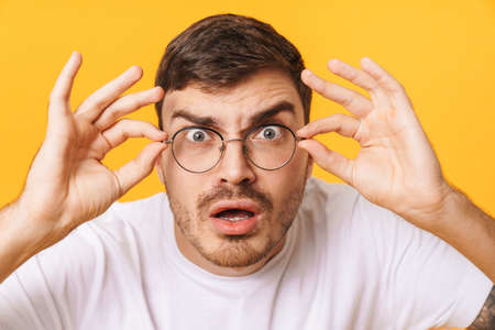 Photo closeup of shocked young man in eyeglasses looking at camera isolated over yellow backgroundの写真素材