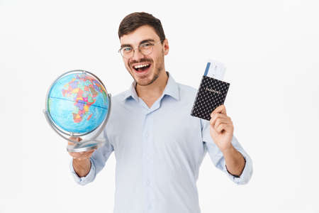 Photo of delighted man in eyeglasses holding passport with tickets and globe isolated over white backgroundの写真素材