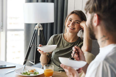 Lovely happy young couple having healthy breakfast in the kitchen, talking