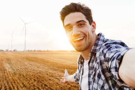 Happy man taking selfie against the industrial landscape with wind turbines