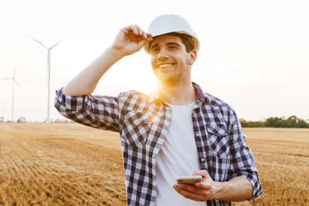 Smiling male engineer using mobile phone while standing at the electric windmill farmの写真素材