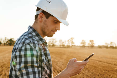 Smiling male engineer using mobile phone while standing at the electric windmill farmの写真素材