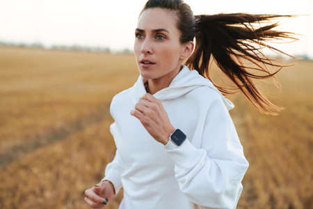 Image of adult beautiful sportswoman running while working out at golden fieldの写真素材