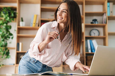 Image of happy adult businesswoman smiling while working with laptop at table in office