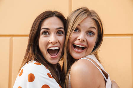 Image closeup of excited adult two women hugging and laughing while posing on city streetの写真素材