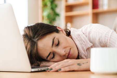 Image of tired adult businesswoman sleeping while working with laptop at table in office